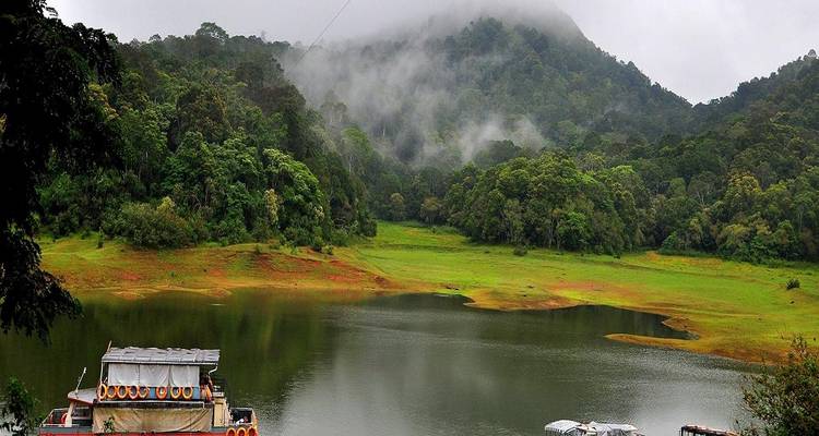 A serene lake surrounded by misty hills and boats in Thekkady.