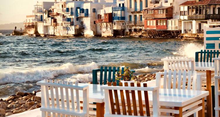 Vista costera en Mykonos con edificios y sillas coloridos.