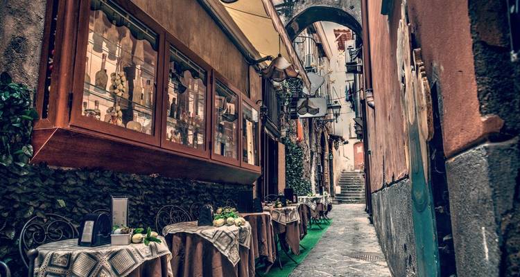 Une ruelle étroite avec des tables de restaurant en plein air.