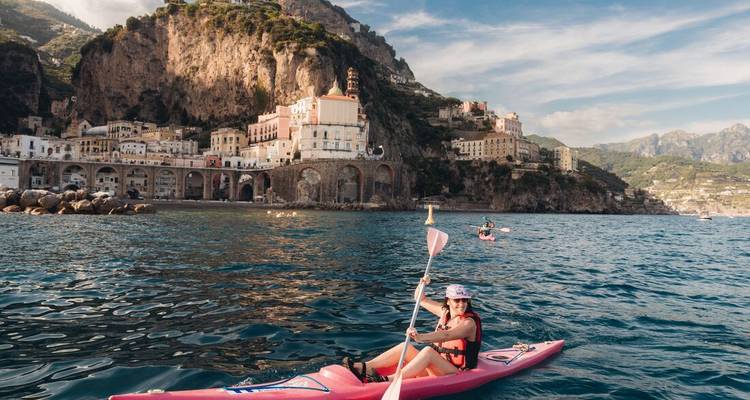 Una persona navegando en kayak en el mar con un pueblo costero al fondo.