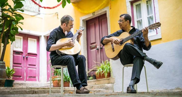 Two musicians play Portuguese guitars in a colorful Lisbon courtyard creating an intimate fado performance.