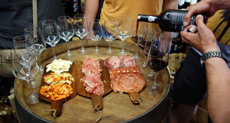 Wine being poured into glasses arranged on a barrel alongside boards of Portuguese cheese and cured meats.