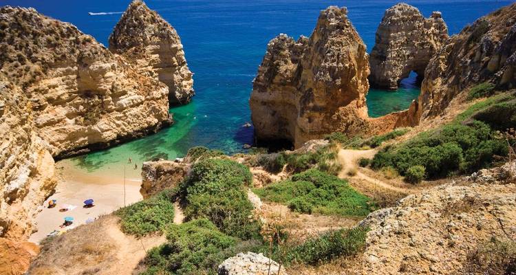 Dramatic limestone cliffs and sea arches framing a secluded turquoise cove and sandy beach on Portugal’s south coast.