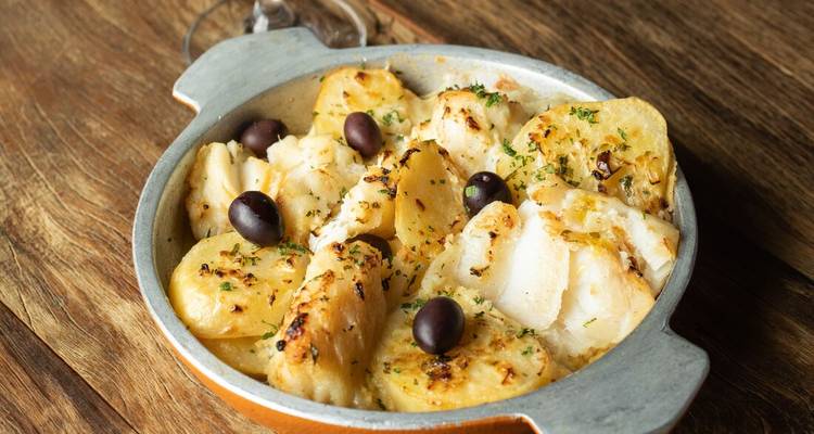 Traditional Portuguese casserole of salted cod, potatoes and olives served in a rustic metal dish.
