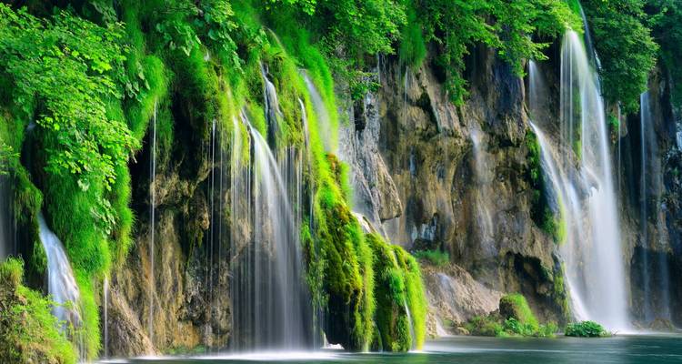Üppige smaragdgrüne Wasserfälle stürzen über moosbedeckte Klippen in einen ruhigen Waldpool.