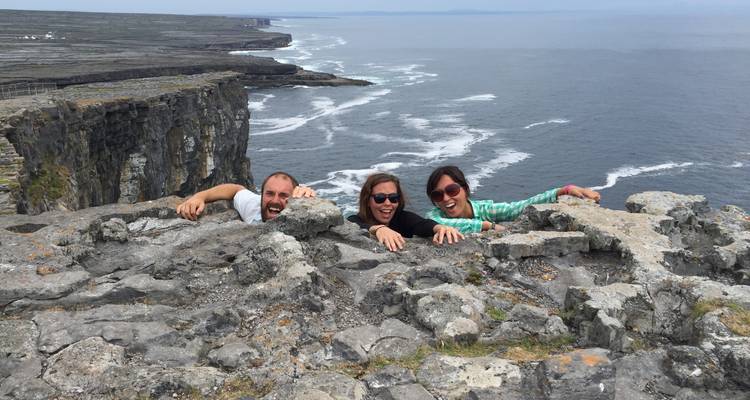 Drie mensen op een rotsachtige klifrand met uitzicht op de oceaan.