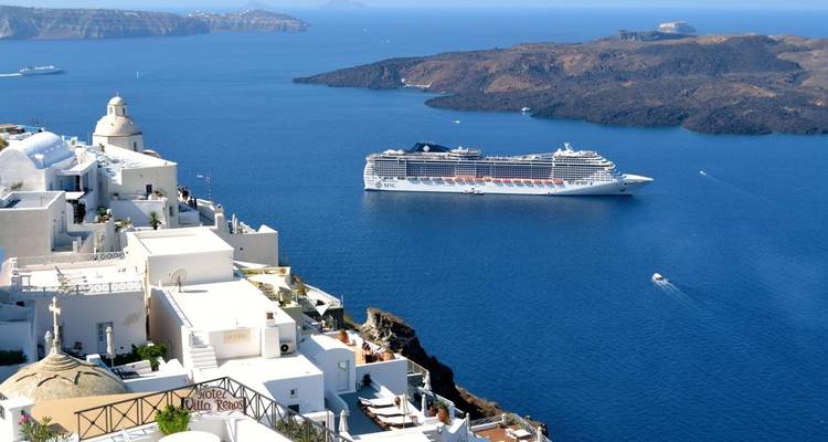 Cruiseschip bij een klifyldorp met witte gebouwen.