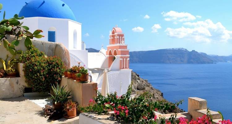 Witte kerk met een blauwe koepel en roze klokkentoren met uitzicht op zee.