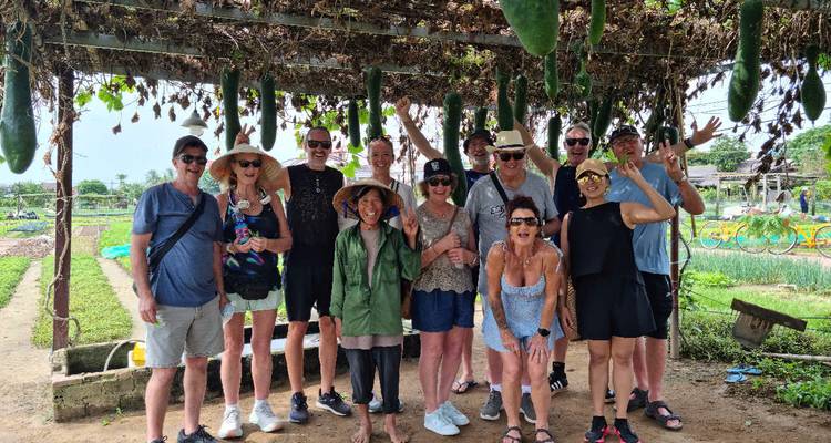 Toeristen die poseren onder een pergola met hangende vruchten in een tuin.