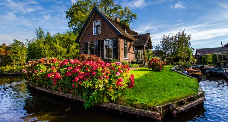 Casita de ladrillo pintoresca con jardín de flores coloridas en un canal en Giethoorn.
