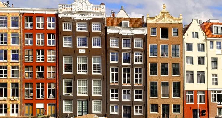 Fila de casas de canal estrechas y coloridas con ventanas grandes contra un cielo brillante