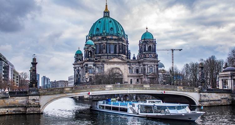 Berlijnse Dom weerspiegeld in de Spree met een rondvaartboot die onder een stenen brug doorvaart.