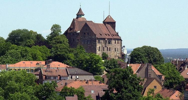 Château en pierre sur une colline entouré d'arbres feuillus et de maisons aux toits rouges par une belle journée