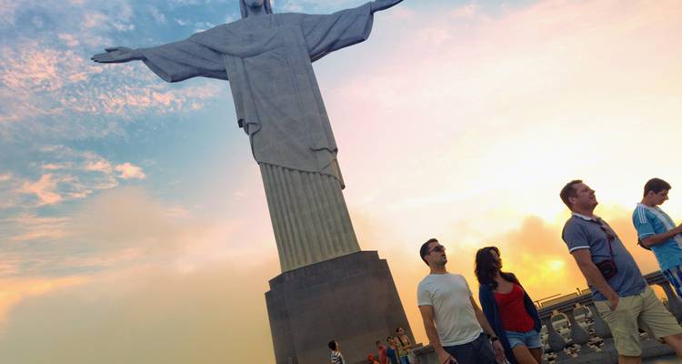 Besucher gehen bei Sonnenuntergang unter der imposanten Statue des Christus des Erlösers hindurch.