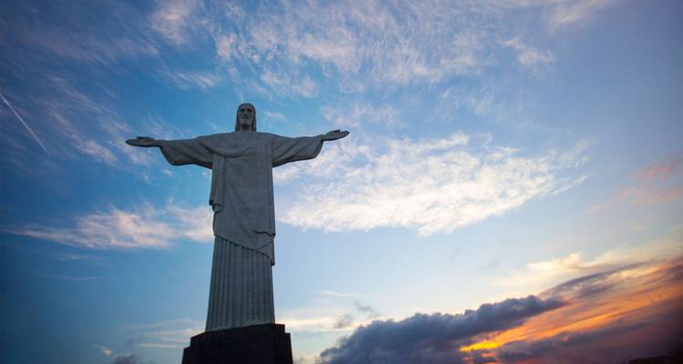Die ikonische Christus-Erlöser-Statue steht gegen einen farbenfrohen Himmel bei Sonnenaufgang.