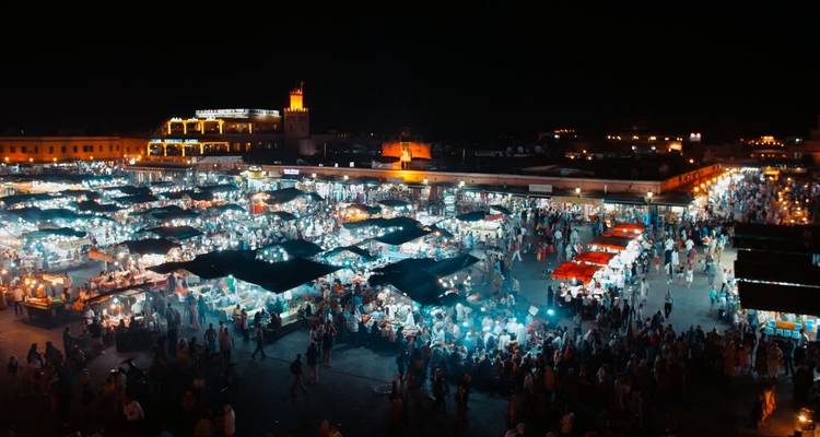 Vista nocturna de una plaza de mercado vibrante con luces y multitudes.