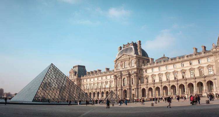 Le Musée du Louvre avec la pyramide de verre et des gens qui marchent.
