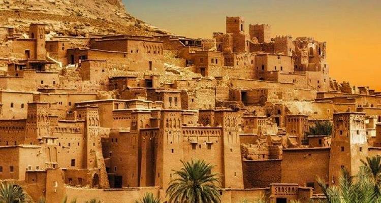 Vue d'Aït Benhaddou avec des bâtiments en argile sous un ciel orange.