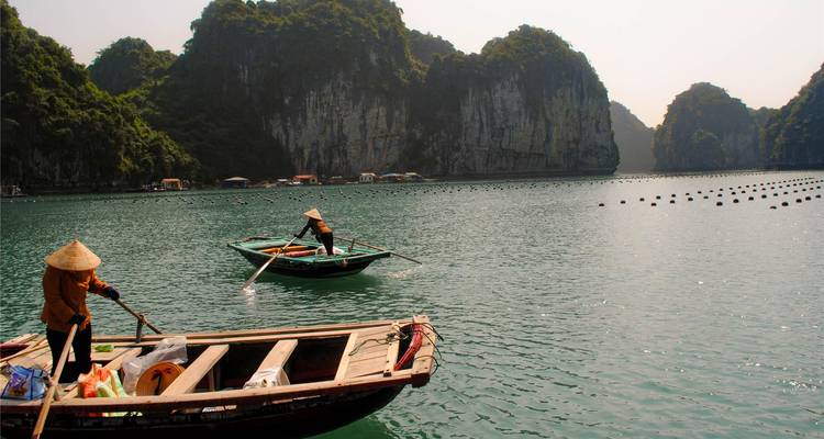 Pescadores con sombreros cónicos reman botes de madera en aguas verdes y tranquilas rodeadas de karst