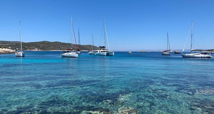 Cala cristalina con veleros anclados e islas verdes bajo un brillante cielo azul croata