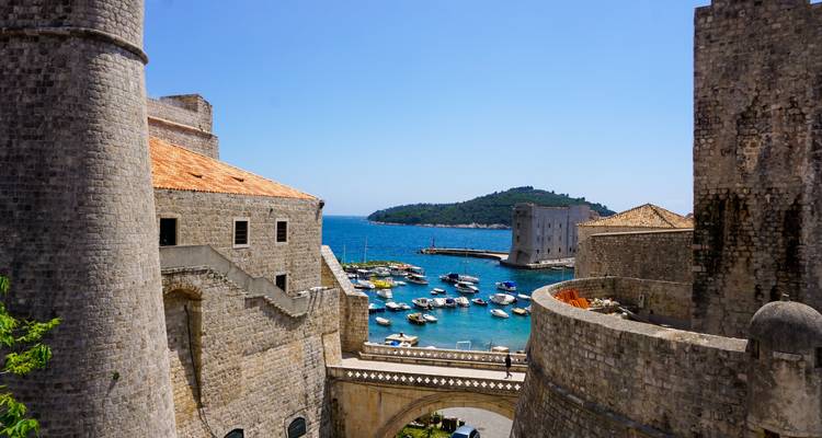 Las fortificaciones de piedra de Dubrovnik que se abren a un pequeño puerto lleno de botes y un horizonte azul