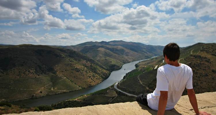 El viajero se sienta en un muro de piedra con vistas al sinuoso río Douro y a los viñedos en terrazas.