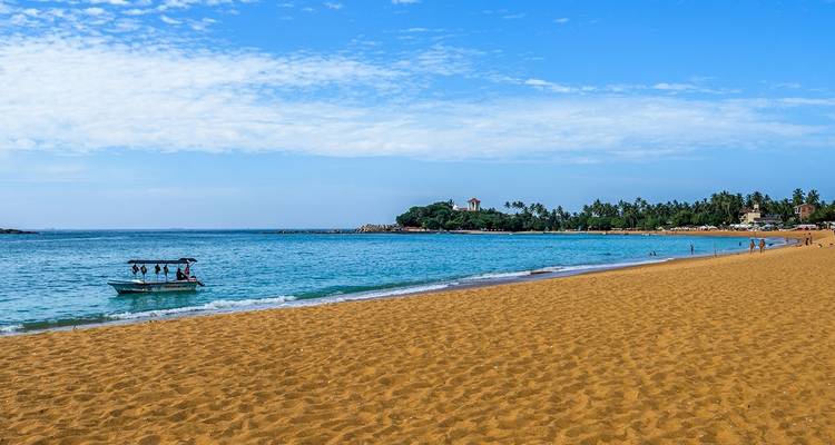 People enjoying a sandy beach with turquoise water and a distant clock tower.