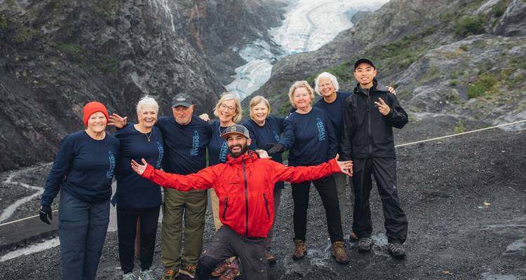 Grupo de senderistas sonriendo posando con un guía en un terreno rocoso muy por encima de un valle de glaciares.