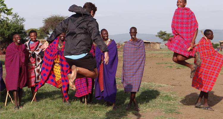 Les hommes Maasai vêtus de shukas colorés sautent haut tandis qu'un voyageur se joint à leur danse traditionnelle sur une clairière du village.