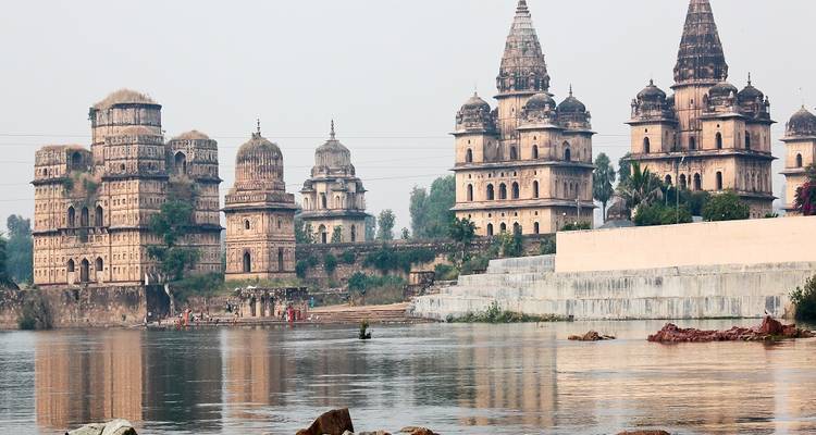 Group of temples and riverbank with people in traditional attire.