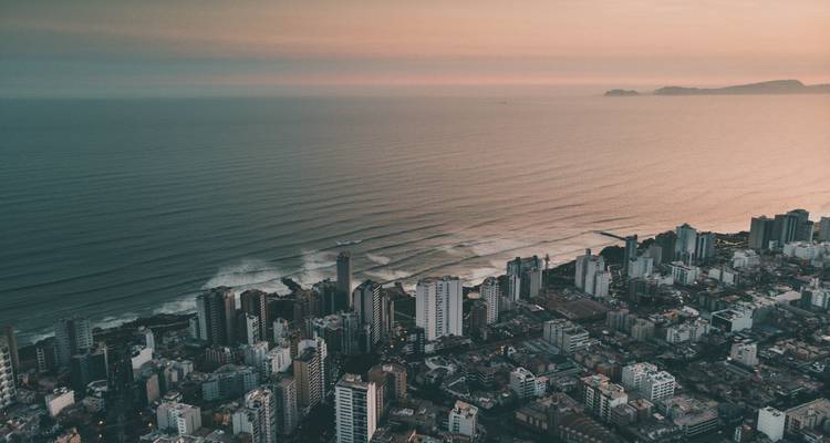 Vue aérienne au crépuscule de la ligne d'horizon d'une ville côtière avec des vagues qui se déroulent vers le rivage