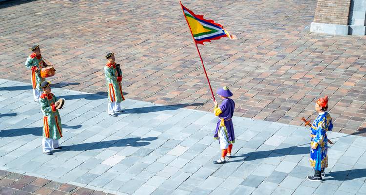 Procesión cultural con artistas en trajes tradicionales sosteniendo una bandera.