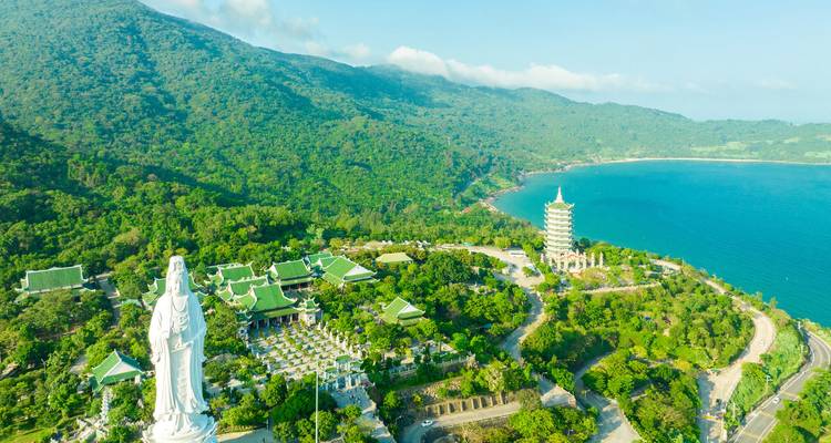 Une grande statue et pagode dans une zone verdoyante luxuriante au bord de la mer.