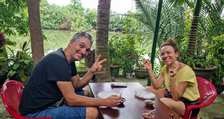 Couple assis à une table en plein air au bord d'une rivière, souriant à l'appareil photo.