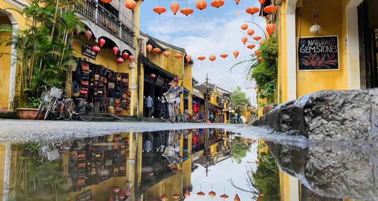 Rue pittoresque avec des lanternes colorées se reflétant dans une flaque d'eau.