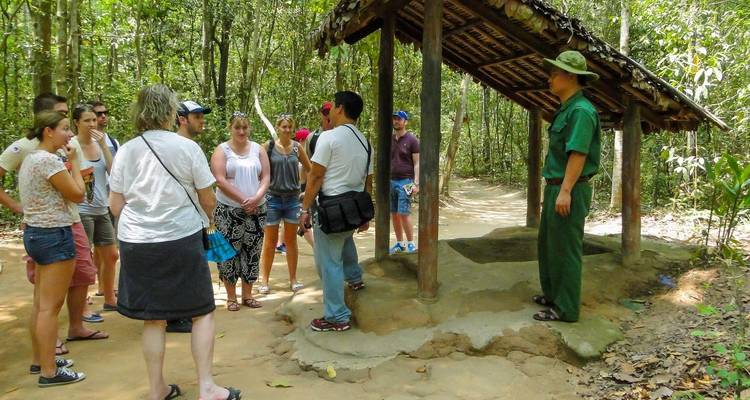 Turistas escuchando a un guía cerca de una zona boscosa con un pequeño refugio.