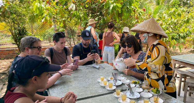 Turistas disfrutando té en una mesa al aire libre rodeada de vegetación.