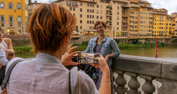 Une voyageuse photographie son amie appuyée sur la balustrade en pierre du Ponte Vecchio avec les bâtiments au bord de l'Arno de Florence en arrière-plan