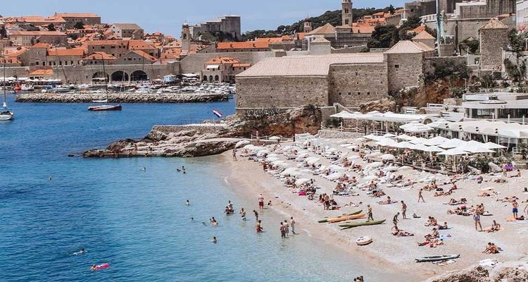 Une plage avec des gens qui se détendent et nagent, avec des structures historiques en arrière-plan.