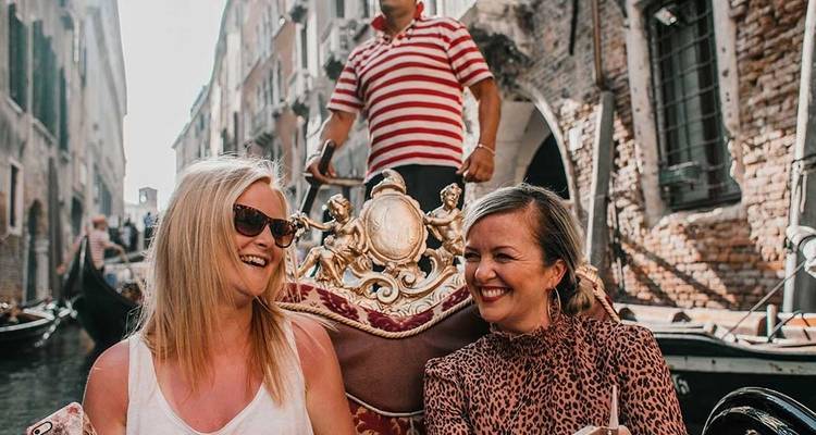 Deux personnes assises dans une gondole naviguant à travers un canal vénitien.