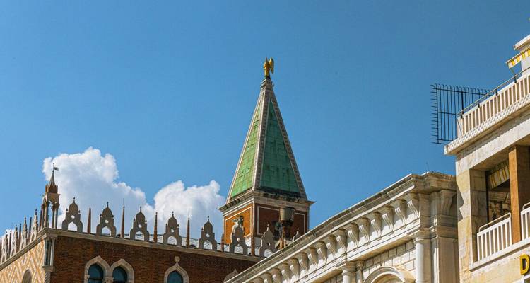 Campanario de cúpula verde y almenas ornamentadas de los tejados de Venecia contra un cielo impecable.