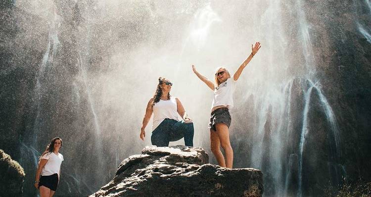 Personas celebrando y posando bajo una cascada con neblina.