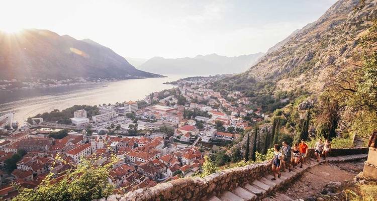 Un grupo de viajeros caminando por una escalinata de piedra con una vista panorámica de un pueblo costero.