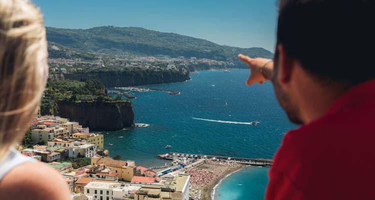 Twee reizigers bewonderen een weids uitzicht op de kust met kleurrijke dorpjes en een turquoise zee