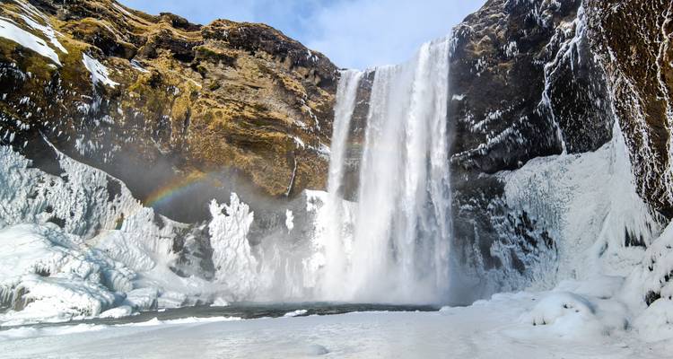 Una amplia cascada con hielo y un arco iris.