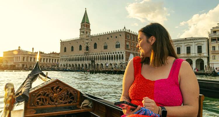 El viajero se relaja en una góndola que pasa junto al Palacio Ducal mientras una luz cálida baña la laguna de Venecia.