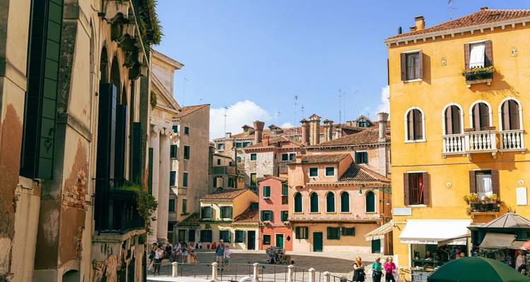 Casas de estuco coloridas y contraventanas enmarcan una tranquila plaza veneciana bajo cielos azules.