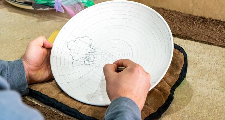 Personne dessinant un motif sur une assiette en céramique blanche.