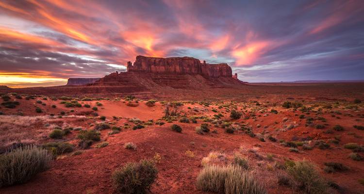 Meseta dramática en Monument Valley bañada en colores vívidos del amanecer bajo un cielo arremolinado