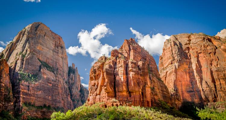 Imponentes acantilados de roca roja del Parque Nacional Zion bajo un cielo azul brillante con nubes esponjosas